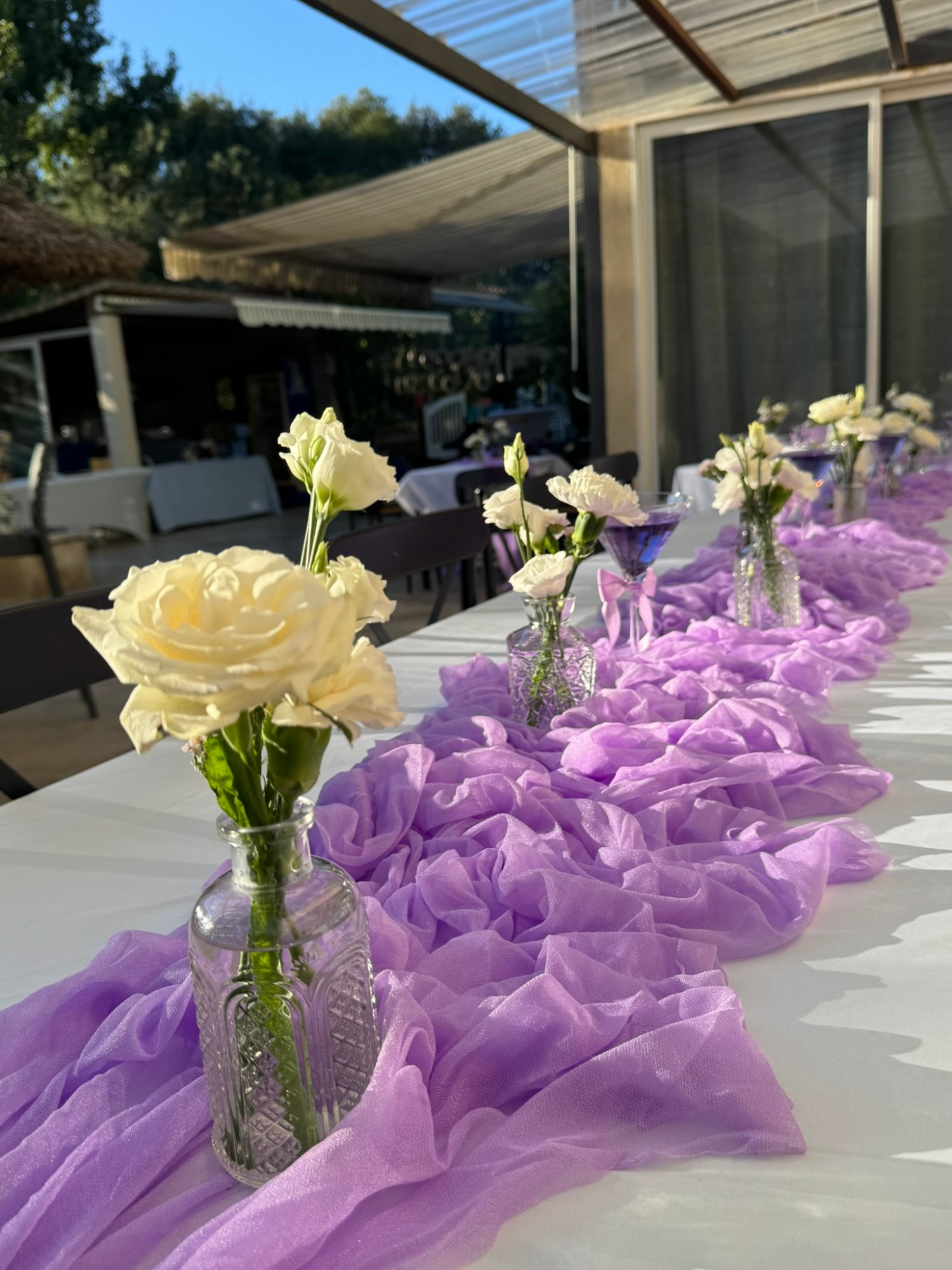 Table d'anniversaire avec chemin de table en voile lilas et soliflores ciselés de roses et œillets blancs