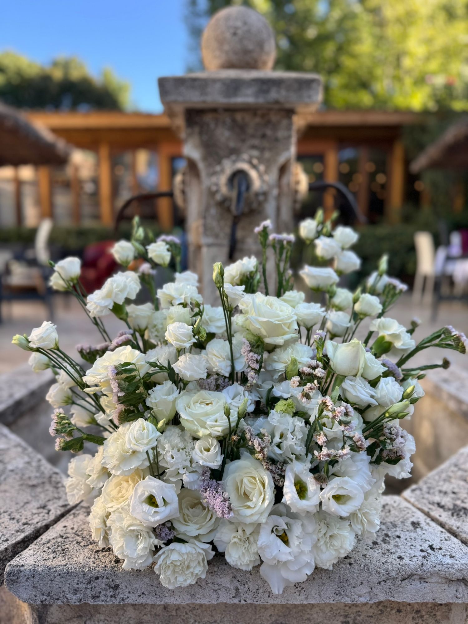 Gros plan sur la composition de roses blanches, lisianthus et statice mauve devant la fontaine