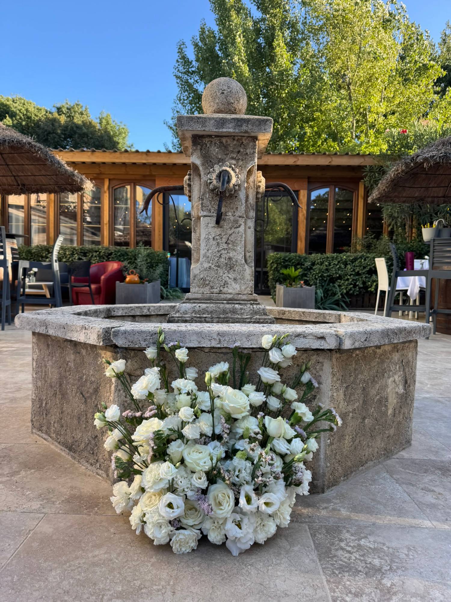 Composition florale de roses blanches, lisianthus et statice au pied d'une fontaine provençale en pierre, anniversaire à Fuveau