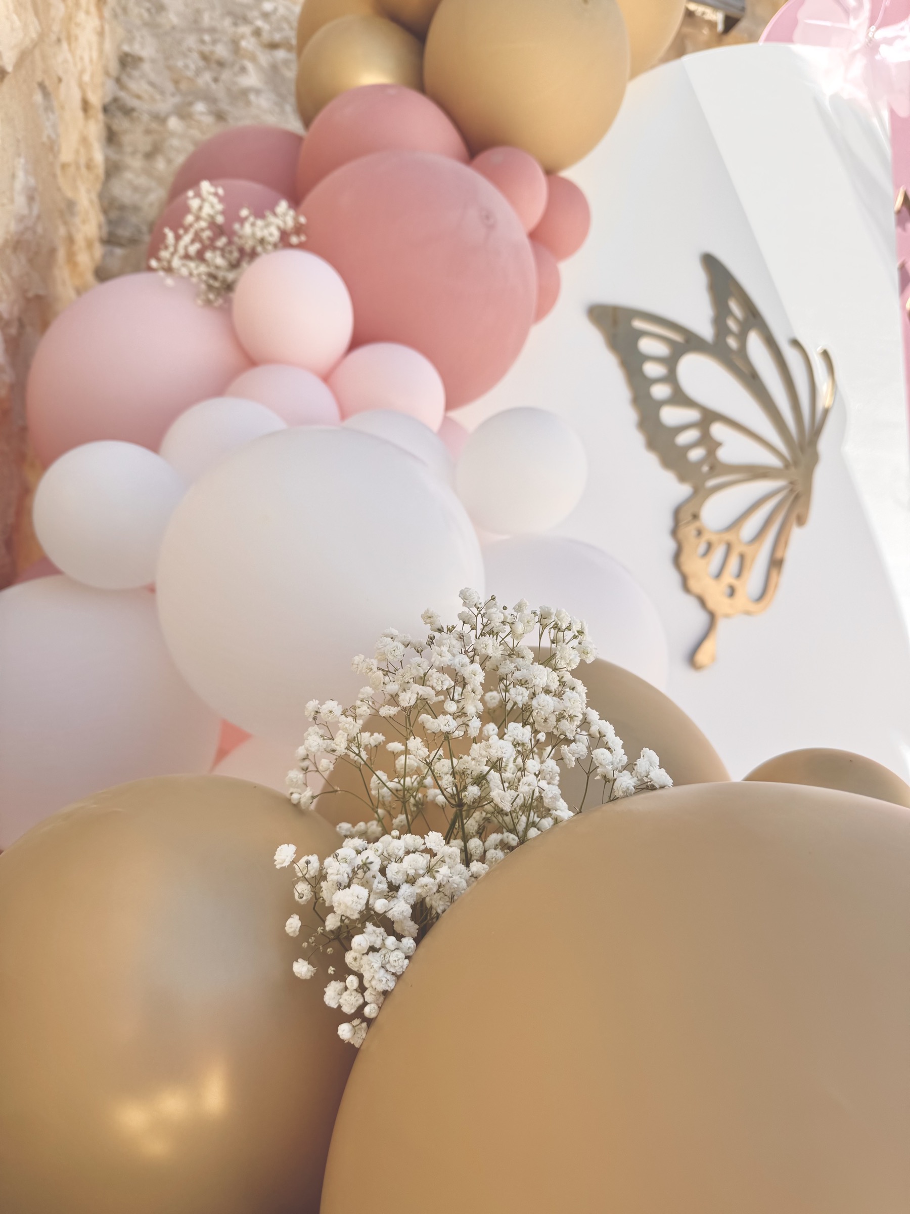 Gros plan ballons rose poudré, nude et doré avec gypsophile et papillon doré — décoration baptême Provence