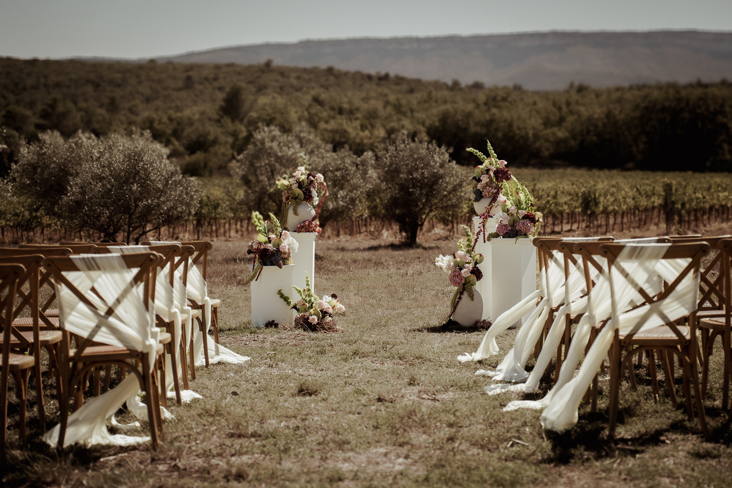 Décoration de cérémonie laïque de mariage entre les oliviers : chaises drapées et colonnes fleuries aux Terres Saint-Hilaire, par Décore tes rêves