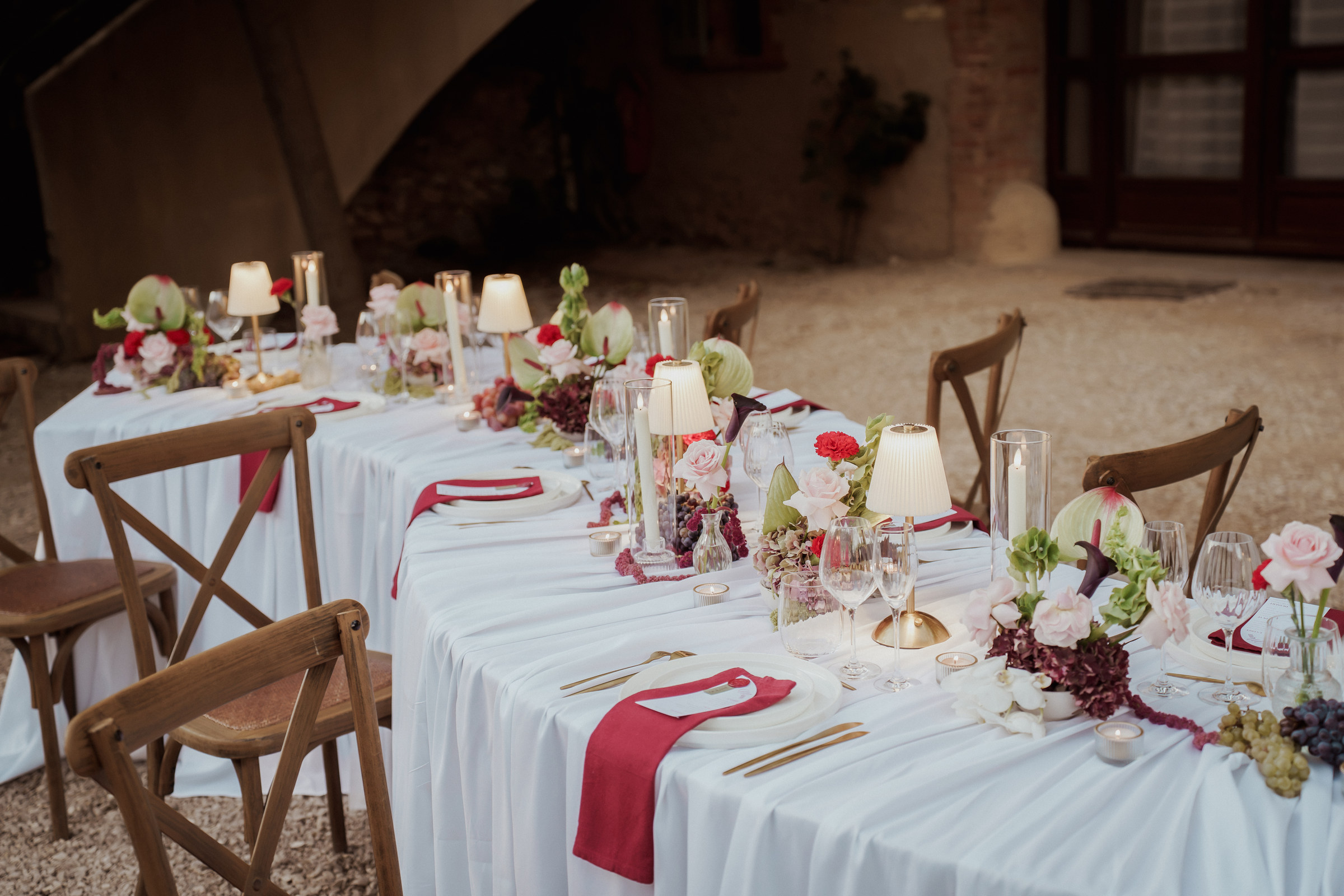 Grande table d'honneur de mariage : nappe blanche, serviettes bordeaux, lampes plissées, bougies, fleurs et grappes de raisin aux Terres Saint-Hilaire