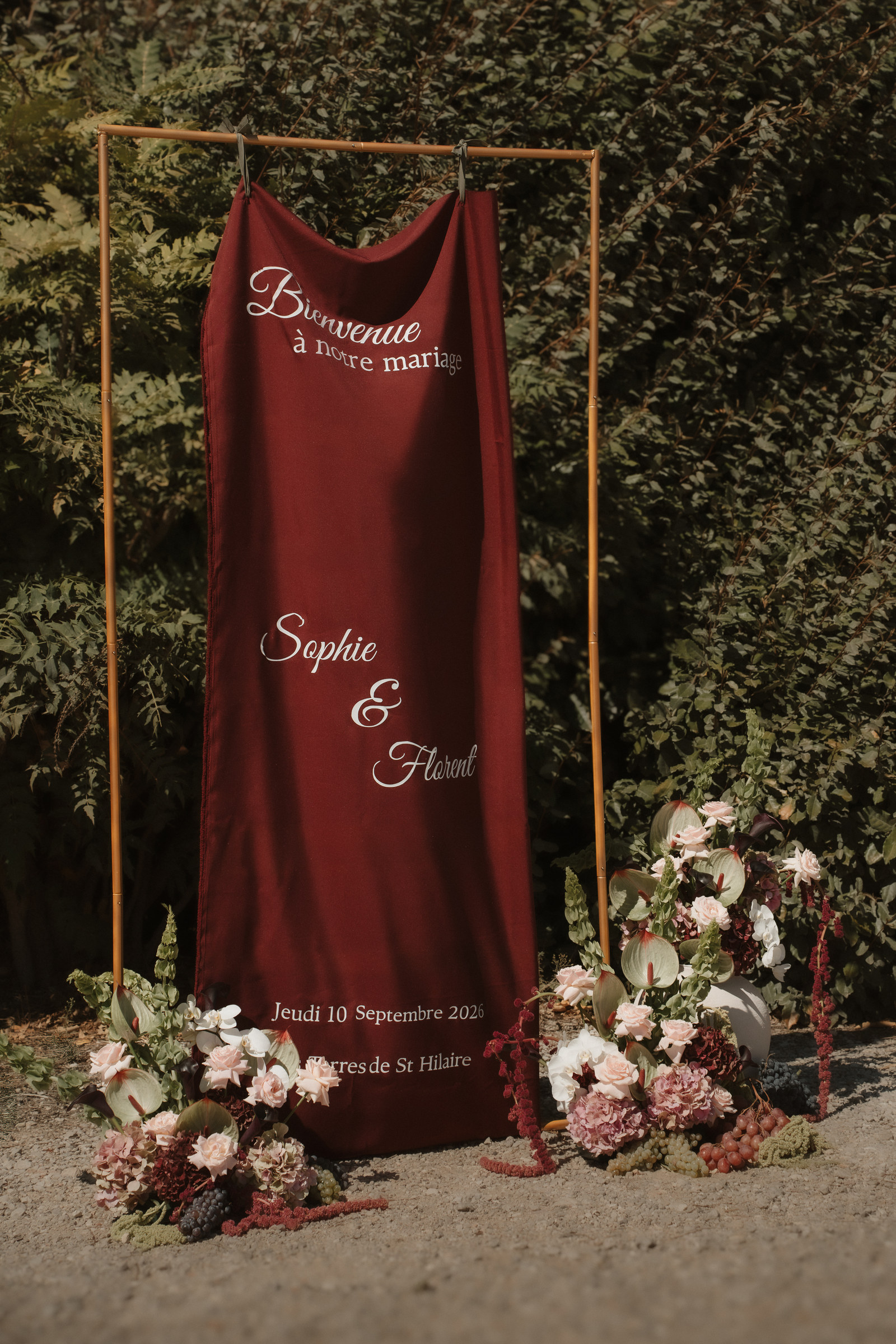 Panneau de bienvenue de mariage en velours bordeaux entouré de compositions florales et de raisin
